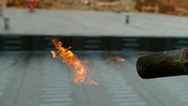 SLOW MOTION, CLOSE UP, DOF: Flames flicker out of the nozzle of a worker's propane torch after laying rolls of bitumen across foundation of a building under construction. Blowtorch is left lit up.