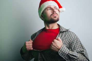 young Santa Claus rips his shirt on his chest like a superhero. the man in the Santa hat,