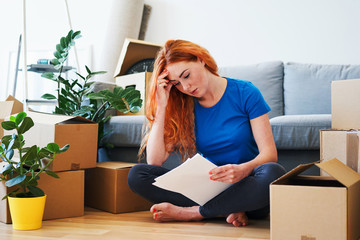 Worried young woman moviing to new apartment looking at bill