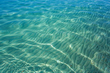 Sunny sea transparent water surface and sandy bottom seen through it. Horizontal color photography.