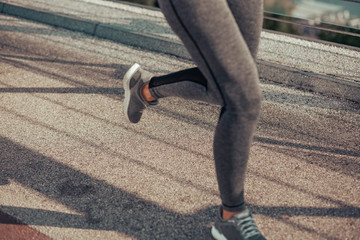 cropped shot of woman in sport wear running on the bridge in the city © Afshar Tetyana