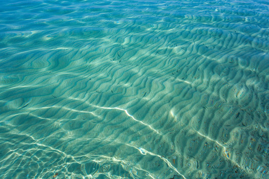 Sunny sea transparent water surface and sandy bottom seen through it. Horizontal color photography.