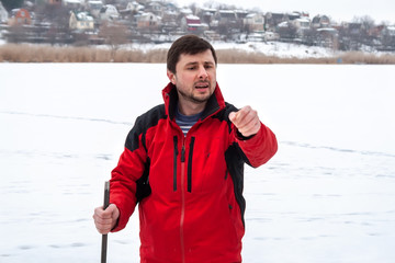 A man in a red jacket with a crowbar in his hands gives instructions, standing on a frozen river....