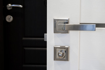 Fototapeta na wymiar Closeup view of an open white wooden door with silver matte metal handle and lock against a blurred dark brown door
