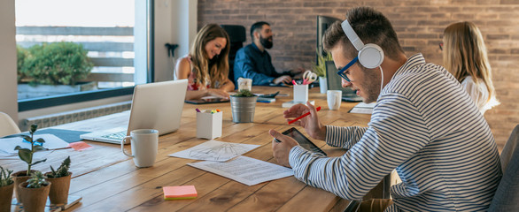 Young man working with tablet and headphones in an office next to his colleagues