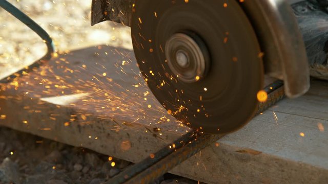 SLOW MOTION, CLOSE UP, DOF: Detailed view of a laborer working at a construction site and cutting into two steel bars with a circular saw. Contractor cutting rusty metal rods with an angle grinder.