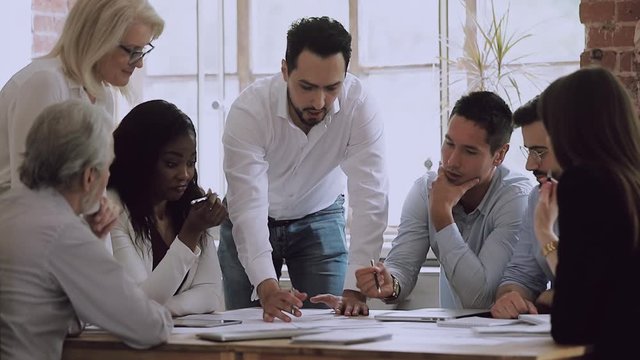 Diverse business team brainstorming on paperwork talking laughing at meeting