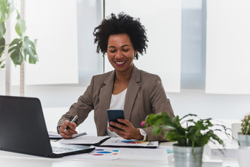 Happy smiling african-american business woman working on laptop at office. Businesswoman sitting at...