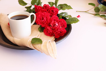 Obraz na płótnie Canvas Hot coffe in awhite cup with natural red roses
