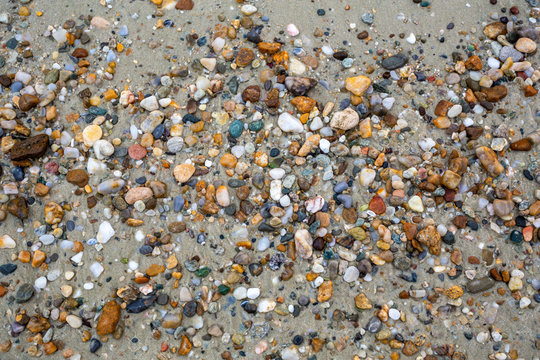 Closeup top view of different colourful vivid stones on sandy beach. Flatlay color photography.