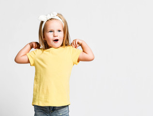 Funny kid baby girl in yellow t-shirt is playing dancing doing exercises with pleasure with her hands on her shoulders