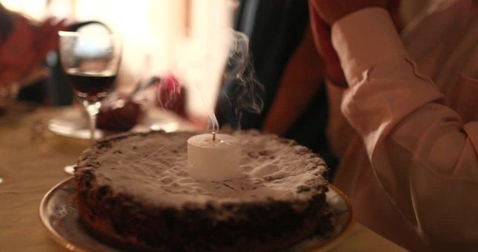 Older man celebrating 70th birthday, senior person blowing birthday candle cake