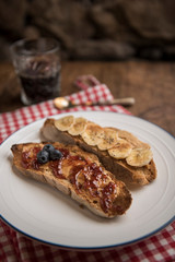 Toasted country loaf with peanut butter, banana, blueberries, cinnamon, maple syrup and strawberry jam. Rustic table and coffee in the background. Vertical, copyspace