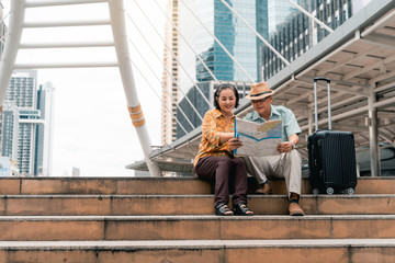 A couple of elderly Asian tourists visiting the capital happily and having fun and looking at the map to find places to visit.
