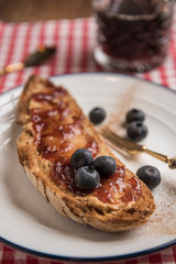 Vegetarian breakfast, toasted rustic bread with peanut butter, strawberry jam, cinnamon and blueberries. Black coffee in the background. Vertical. Closeup