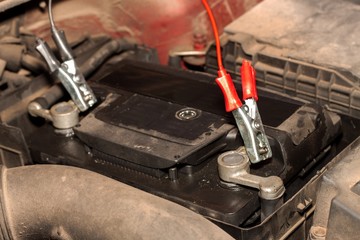 Charging an old car battery in a dirty engine. Preparing the car for winter season. Faulty car battery.