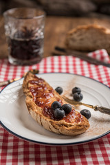 Rustic table with vegan breakfast. Slice of rustic bread with peanut butter, strawberry jam, cinnamon and blueberries. Bread and black coffee in the background. Vertical. Selective focus