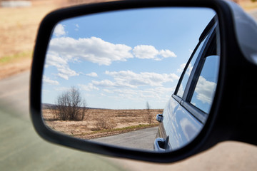 Side view mirror reflection of landscape with road and sky with clouds in sunny spring or autumn day