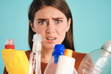 Close up scared girl with empty plastic detergents amazedly looking in camera over colorful background isolated