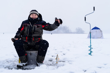 Fototapeta na wymiar Happy smiling adult fisherman is holding catched fish after successful winter fishing at cold winter day