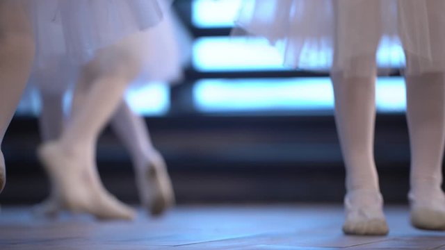 Close-up of a girl's legs in white ballet shoes on an old wooden floor during ballet training. Element of classical dance exercise.