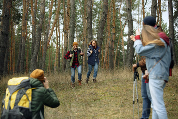 Fototapeta premium Group of friends on a camping or hiking trip in autumn day. Men and women with touristic backpacks going throught the forest, talking, laughting. Leisure activity, friendship, weekend.