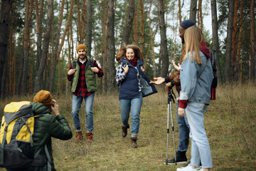 Group of friends on a camping or hiking trip in autumn day. Men and women with touristic backpacks going throught the forest, talking, laughting. Leisure activity, friendship, weekend.