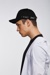 Cropped side photo of a dark-haired man, wearing black baseball cap with lettering "the most common" on the left side of a cap, black t-shirt and white shirt. 