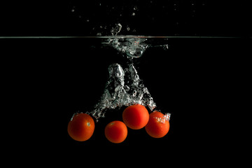 Four small tomatoes falls under water with splash