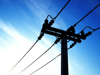 Silhouettes high-voltage wires on a pole - closeup. On a background of blue sky with sunshine in...