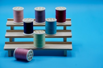 A group of pink, purple, blue, green and red thread on the wooden stand on the blue background
