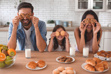 portrait of mother, daughter and father covering eyes with cookies on the kitchen