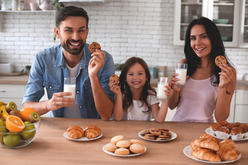 smiling family looking at the camera and holding cookies with milk glasses in the kitchen