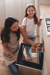 overhead view of woman taking muffins from the oven and girl looking at the camera