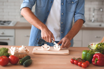 cropped shot of man cutting mushrooms on cutting board in the kitchen
