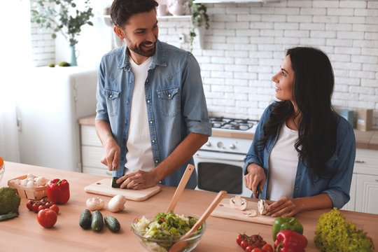 Smiling Woman And Man Cooking Salad In The Kitchen Together