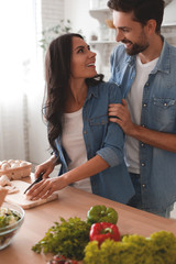 husband embracing wife cutting mushrooms on the wooden board and looking at each other