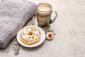 Hot coffee with a donut. Winter drink for a good mood with sweater, leaves and flowers. Old wood plank background