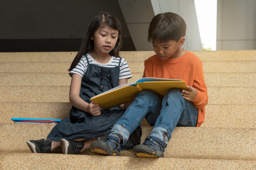 Two asian children,boy and girl siit on stair at school,reading book,fun and happy,education concept,learning and knowlage.