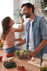 happy father and daughter tasting freshly prepared salad on the kitchen