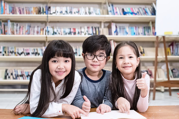 The little boy sitting at the middle of two smart grils,reading book together,at library,blurry light around