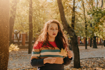 Beautiful Plus size woman in a bright striped sweater walking in the fall autumn city park. Autumn...