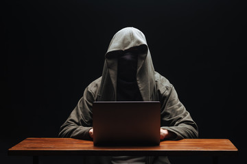Hacker without a face in a hood with a laptop on a black background