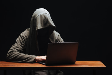 Hacker without a face in a hood with a laptop on a black background