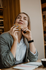 Lifestyle Portrait of smiling young casual blonde woman eating a cookie and drinking coffee, tea in cafe. Happy girl eating a dietetic gluten free cookie