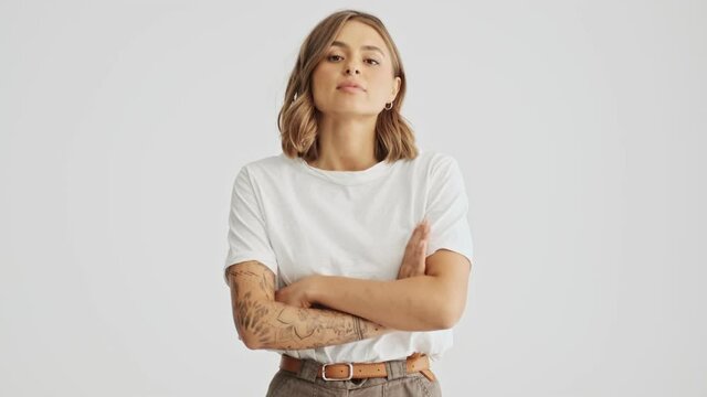Attractive young woman wearing a white basic t-shirt comes in and looking seriously with arms folded isolated over white background