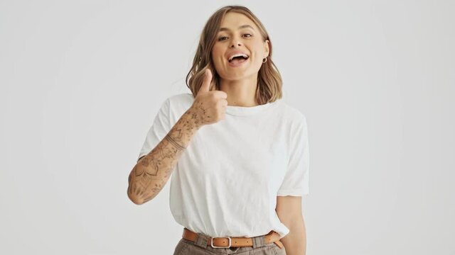 Successful young woman wearing basic t-shirt comes in then showing thumbs up gesture isolated over white background