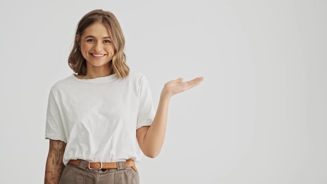Pretty young woman wearing basic t-shirt presenting something using her hand isolated over white background