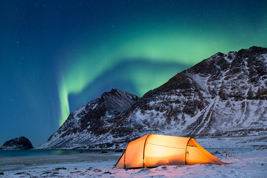 Illuminated tent on Lofoten islands under northern lights in winter