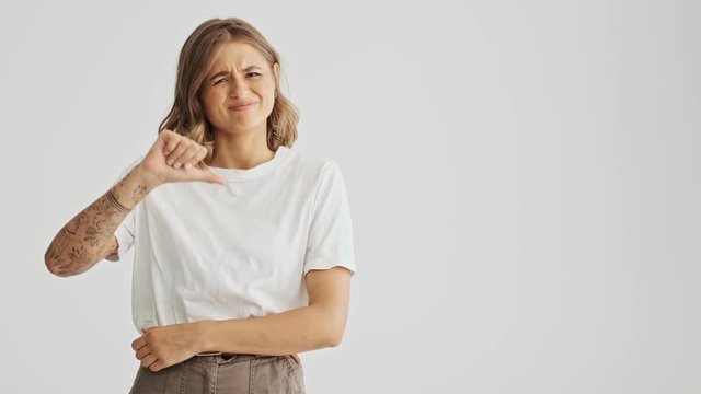 Pretty young woman wearing a basic t-shirt showing thumb down then up isolated over white background